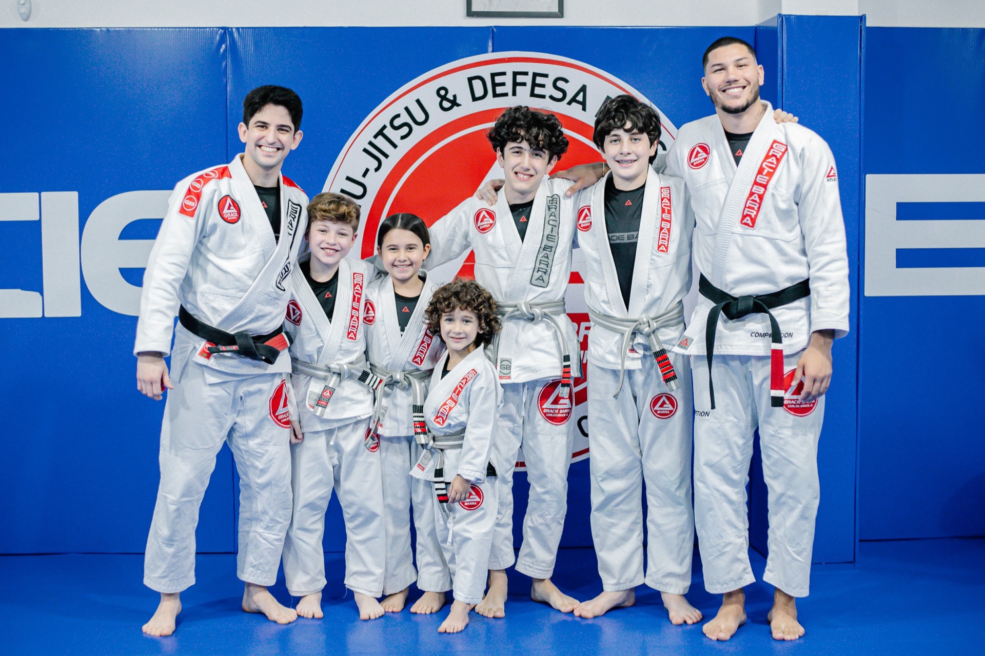 Instrutores e crianças da Gracie Barra Tubarão posando diante do escudo Gracie Barra